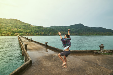 Traveling boy on the pier. Pretty young man jumping on the bridge. Summer lifestyle and adventure photo