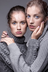 Two young women in gray sweaters on grey background. Beautiful girls stretching hands forward in embrace. Female friendship concept