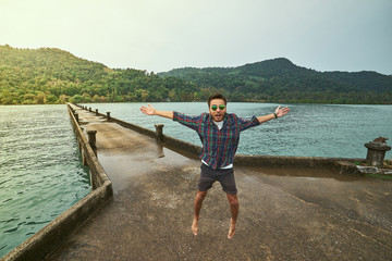 Traveling boy on the pier. Pretty young man jumping on the bridge. Summer lifestyle and adventure photo