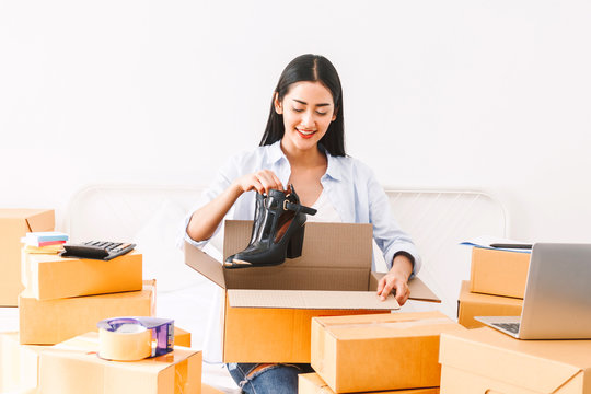 Young woman freelancer working sme business online shopping and packing shoes with cardboard box on bed at home - Business online shipping and delivery concept
