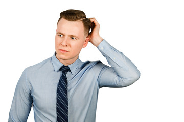 Young thinking businessman dressed in blue shirt and tie scratches his head, isolated on white background
