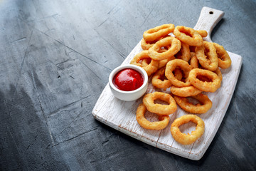Fried Onion Rings with Ketchup on white cutting board.