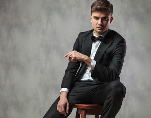 sexy gentleman dressed elegantly sitting and pointing to side