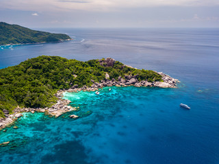 Drone view of a boat in a clear ocean next to tree covered tropical islands (Similan Islands, Thailand)