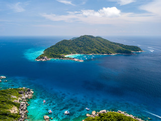 Aerial view of boats over a stunning tropical coral reef next to jungle covered desert islands