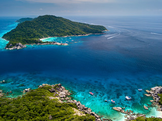 Aerial view of boats over a stunning tropical coral reef next to jungle covered desert islands