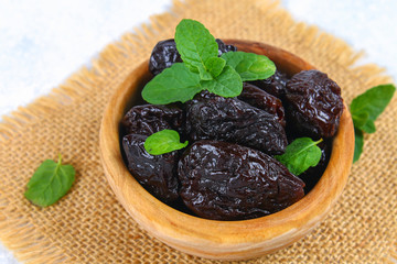 Prunes and fresh mint leaves in a bowl on a concrete table.