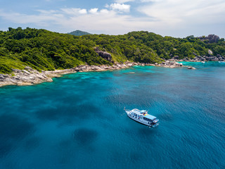 Drone view of a boat moored next to a tree covered tropical desert island