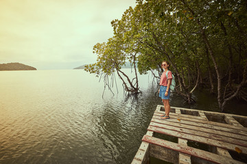Traveling girl on the wood pier. Pretty young woman with backpack and tropical landscape. Summer lifestyle and adventure photo. Fish eye lens image