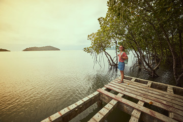 Traveling girl on the wood pier. Pretty young woman with backpack and tropical landscape. Summer lifestyle and adventure photo. Fish eye lens image