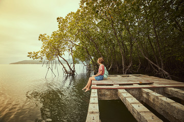 Fototapeta na wymiar Traveling girl on the wood pier. Pretty young woman with backpack and tropical landscape. Summer lifestyle and adventure photo. Fish eye lens image