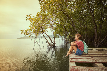 Traveling girl on the wood pier. Pretty young woman with backpack and tropical landscape. Summer lifestyle and adventure photo. Fish eye lens image