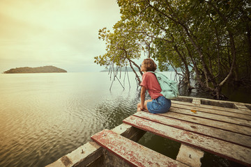Fototapeta na wymiar Traveling girl on the wood pier. Pretty young woman with backpack and tropical landscape. Summer lifestyle and adventure photo. Fish eye lens image