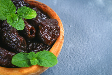 Prunes and fresh mint leaves in a bowl on a concrete table.