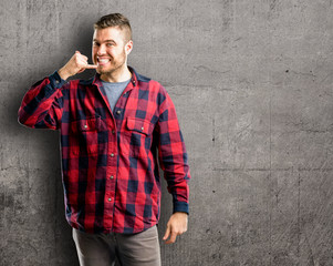 Young handsome man happy and excited making showing call me gesture with hand shaped like telephone