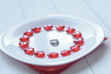 close up.ring and red hearts on a white plate