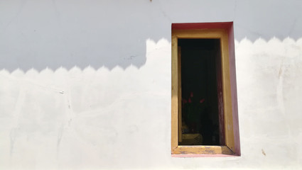 white temple wall with single window and roof shadow