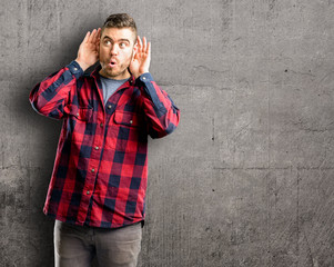 Young handsome man holding hand near ear trying to listen to interesting news expressing communication concept and gossip