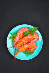 Large royal raw frozen prawns on a blue plate with thyme and basil on a concrete table. Red shrimps. Top view.