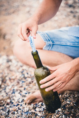 man in denim shorts puts a note in the bottle on the beach in the summer