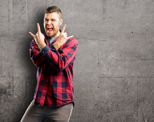 Young handsome man making rock symbol with hands, shouting and celebrating