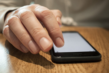 Close up of man using a smart phone on wooden desk