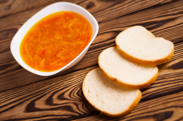 One full white ceramic bowl of fresh hot vegetable borscht and three pieces of bread on old weathered rustic wooden table. Ukrainian national food