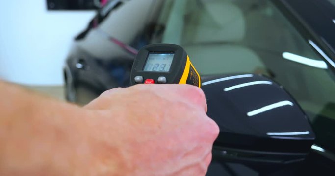 The professional worker holds a pistol in his hand measuring the temperature of the auto repair shop, car washing.