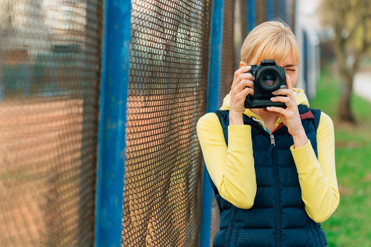 Girl with professional camera in hands. Close up of female photographer doing photos in park.