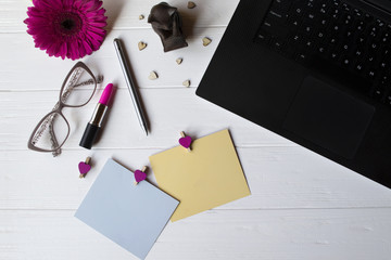 Laptop, colorful memo sheets, eyeglasses, stylus, pink gerbera and elements of decoration on a white wooden work desk. Beautiful female workplace top view.