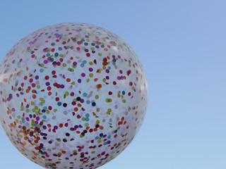 Multi colored confetti filled balloon against bright clear blue sky no clouds