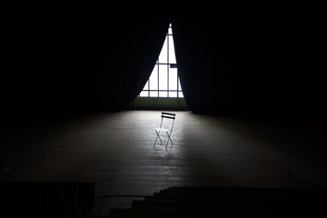 Scène de théatre dans le noir avec juste un rayon de lumière qui éclaire une chaise vide