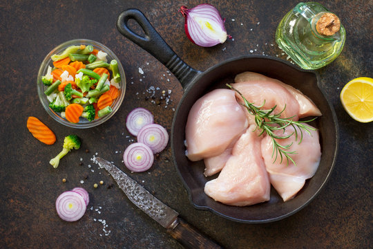 Fresh meat. Raw chicken fillet on a cast iron frying pan, spices and fresh vegetables on a kitchen table. Top view flat lay background.