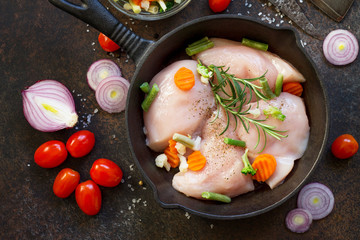 Fresh meat. Raw chicken fillet on a cast iron frying pan, spices and fresh vegetables on a kitchen table. Top view flat lay background.