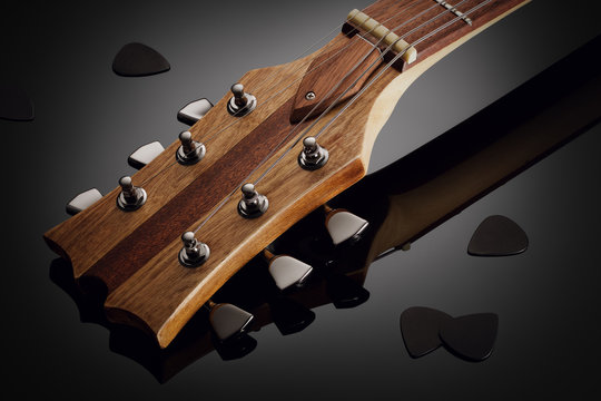 Close up on the headstock of custom guitar, black picks around, glossy background with reflection