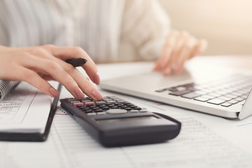 Closeup of woman hands counting on calculator and typing on laptop