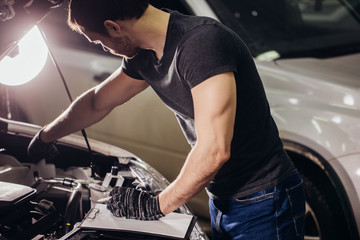 Obraz na płótnie Canvas Mechanic examining under hood car and writing notes at repair garage
