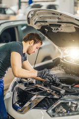 Auto mechanic working under car hood in repair garage