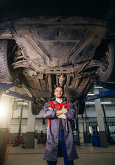 Portrait of mechanic under lifted car loking at camera and crossed hands