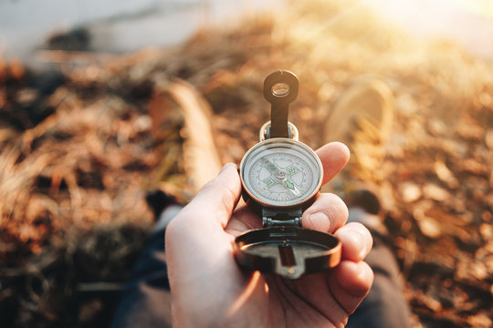 Hipster traveler hold vintage compass in hand on background of him legs in hiking boots. Flare effect