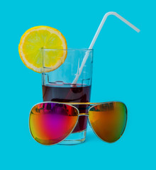 Fresh Juice glass with a straw slice of yellow lemon and sunglasses on a blue background. Fashion pastel summer design style concept