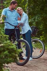 Obraz premium An attractive couple of a blonde female and man dressed in casual clothes on a bicycle ride in the park.