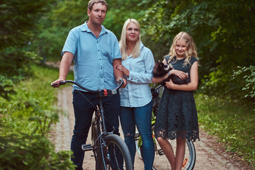 Obraz premium Attractive family dressed in casual clothes on a bicycle ride with their cute little spitz dog.