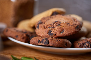 Side view of chocolate chip cookies on a wooden plate over rustic background, selective focus