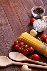 Uncooked pasta, tomatoes and spice on wooden background, top view, close-up, selective focus