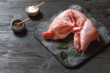 Whole Forest wild rabbit, Raw meat with spices and vegetables, Sea salt, red, white pepper and coriander in clay pots on an old black rustic table, copy space © jarvna