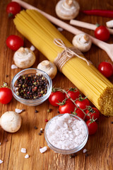 Uncooked pasta, tomatoes and spice on wooden background, top view, close-up, selective focus