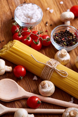 Uncooked pasta, tomatoes and spice on wooden background, top view, close-up, selective focus