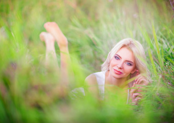 Naklejka na ściany i meble Smiling beautiful young woman resting among green grass