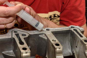 Car mechanic repairs car engine in workshop, apply sealant